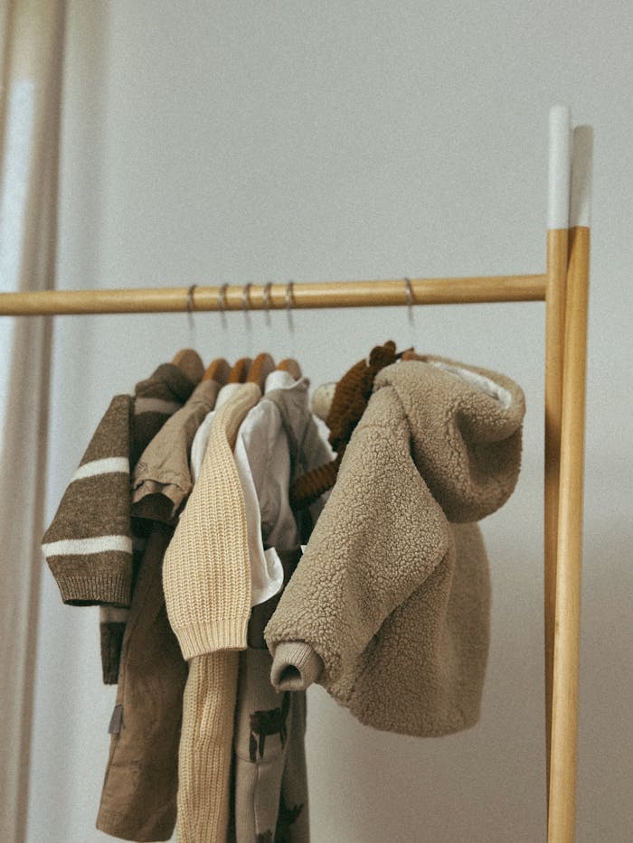 A selection of brown and beige childrens clothing hanging on a wooden rack indoors.